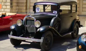 Auto storica nera, un vero gioiello che dimostra quanti anni ha un'auto d'epoca. Accanto, un'auto rossa sportiva.