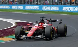 Un'auto di F1 in gara, con livrea rossa Ferrari, sfreccia in curva. La pubblicità "American Express" fa da sfondo a questa emozione da vedere in TV.