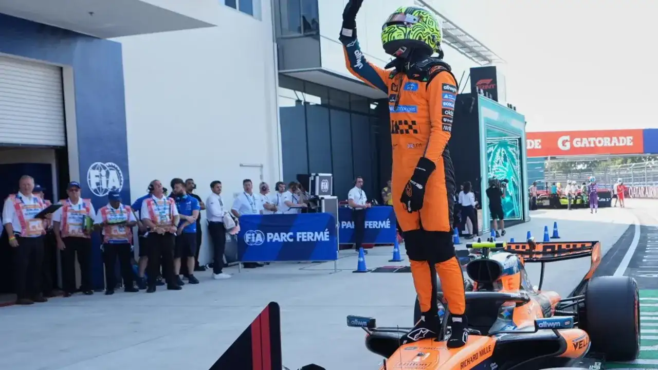 Pilota McLaren in tuta arancione saluta dal podio del GP Miami, con il team FIA Parc Fermé sullo sfondo.