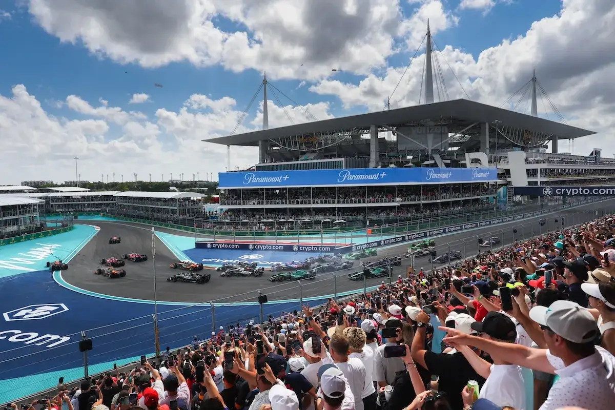 Vetture di Formula 1 sfrecciano sul circuito durante il GP Miami, con tribune gremite di tifosi entusiasti e lo stadio sullo sfondo.