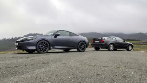 Due coupé Honda, una moderna e una classica, si incontrano su una strada di campagna. La nuova Honda Prelude 2026, grigio scuro, spicca accanto alla sua antenata.