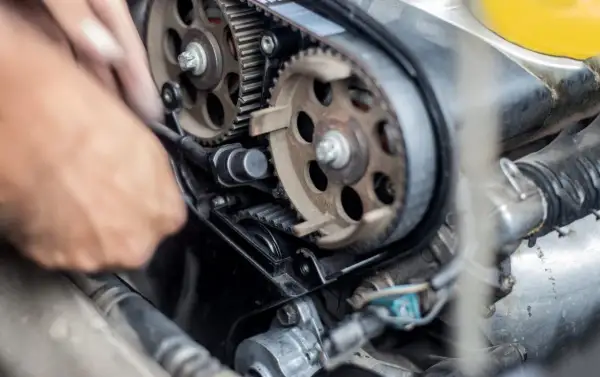 Mano che lavora per cambiare cinghia distribuzione motore auto, con ingranaggi e pulegge in primo piano.