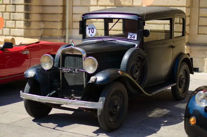 Auto storica nera, un vero gioiello che dimostra quanti anni ha un'auto d'epoca. Accanto, un'auto rossa sportiva.
